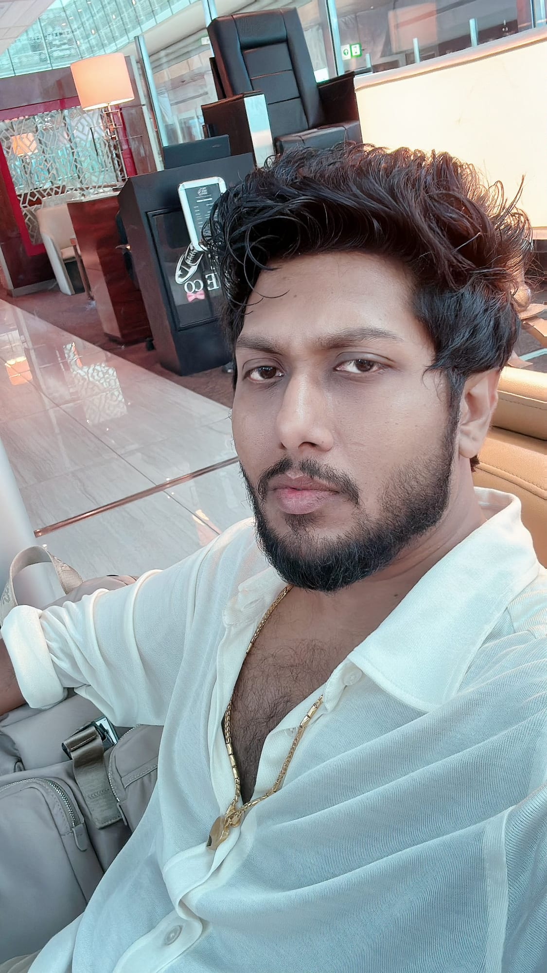 Vinay Anuragh in a sheer white shirt and gold chain, seated in a lounge